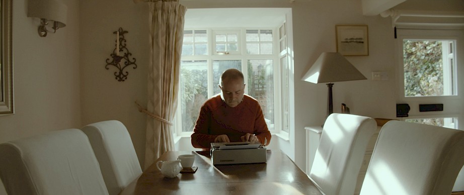 Arthur sitting in front of his typewriter with a cup of tea next to him.